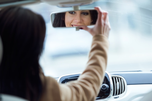 Mooie jonge vrouw die achteruitkijkspiegel van de auto bevestigt.