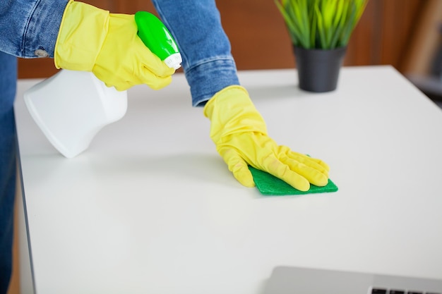 Mooie jonge vrouw die beschermende handschoenen draagt die het bureau in bureau schoonmaken