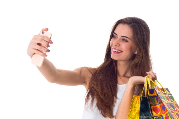 Mooie jonge vrouw die boodschappentassen vasthoudt en selfie maakt op een witte achtergrond in de studio