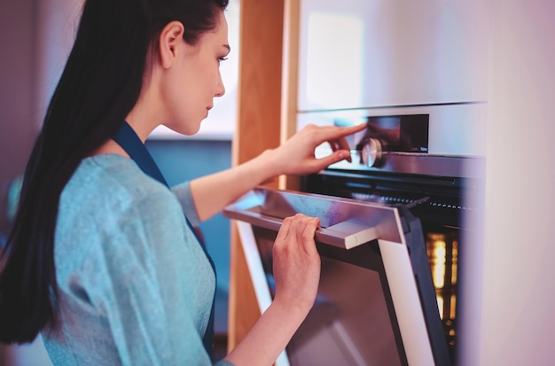 Mooie jonge vrouw die controleert hoe haar cake het doet in de oven