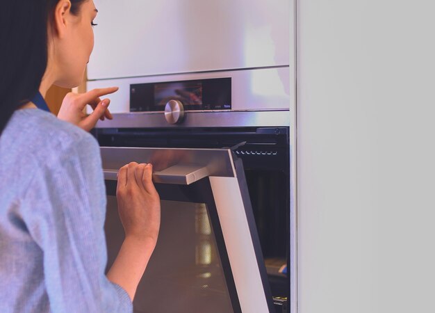 Mooie jonge vrouw die controleert hoe haar cake het doet in de oven