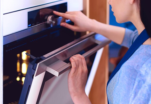 Mooie jonge vrouw die controleert hoe haar cake het doet in de oven