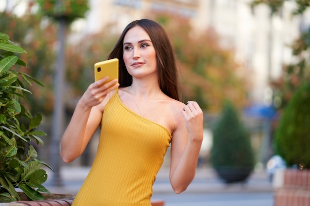 Mooie jonge vrouw die een audio verzendt met haar smartphone, met gele telefoon en jurk