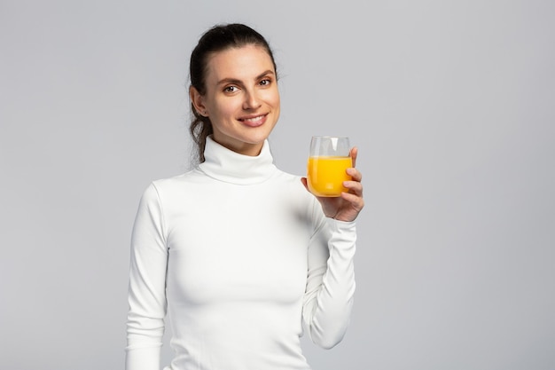 Mooie jonge vrouw die een glas sinaasappelsap drinkt, gezonde levensstijl op lichtgrijze achtergrond