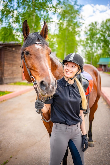 Mooie jonge vrouw die een helm draagt die haar bruine paard aait