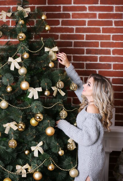 Mooie jonge vrouw die een Kerstboom verfraait terwijl het wachten op een Kerstmisvakantie