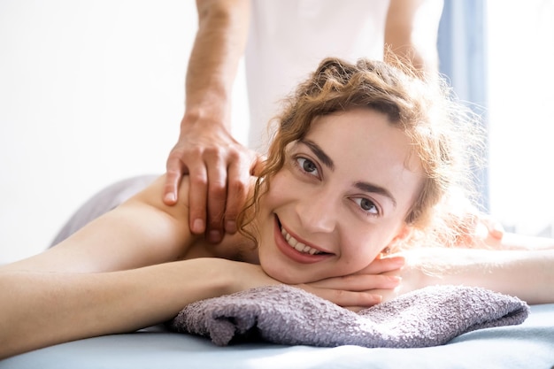 Foto mooie jonge vrouw die een lichaamsmassage krijgt en naar de camera glimlacht