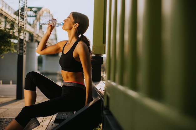 Mooie jonge vrouw die een pauze neemt tijdens het sporten buiten en het drinken van water