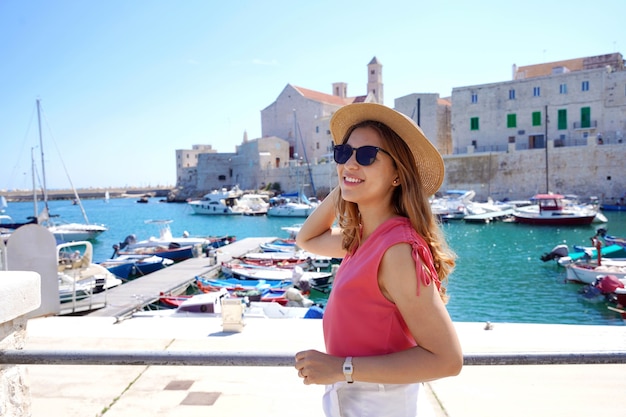 Mooie jonge vrouw die een zonnebril draagt die dichtbij de oude haven van Giovinazzo, Apulië, Italië loopt