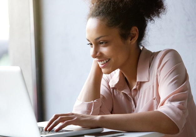 Mooie jonge vrouw die en laptop het scherm glimlacht bekijkt