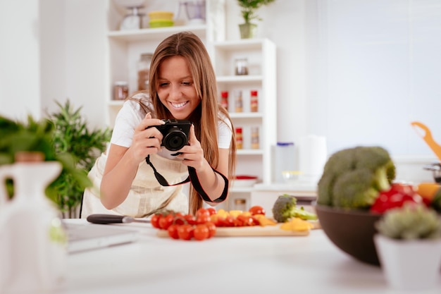 Mooie jonge vrouw die foto's maakt van gezonde salade met digitale fotocamera voor haar blog.