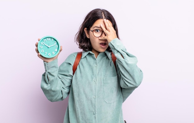 Mooie jonge vrouw die geschokt, bang of doodsbang kijkt en haar gezicht bedekt met de hand. wekker concept