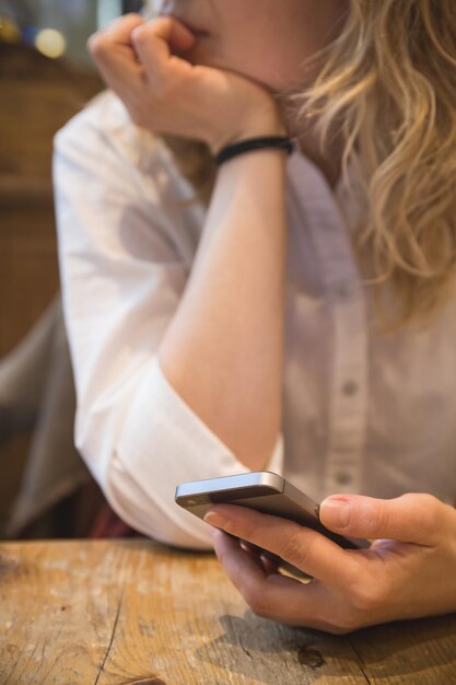 mooie jonge vrouw die gezellig aan een houten tafel zit en een smartphone met touchscreen gebruikt