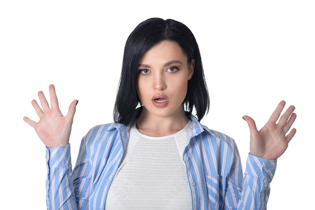 Mooie jonge vrouw die gezichtsuitdrukking maakt die tegen witte achtergrond stelt
