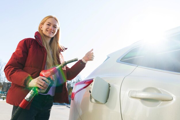 Mooie jonge vrouw die haar auto bij zonnig weer bijtankt