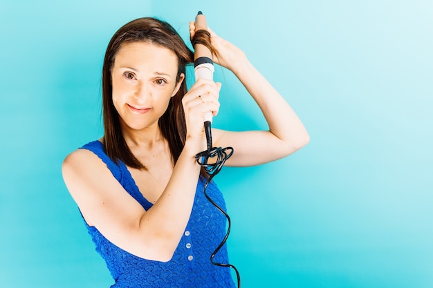 Mooie jonge vrouw die haar haar met een blauwe achtergrond van een haarkrulspeld droogt