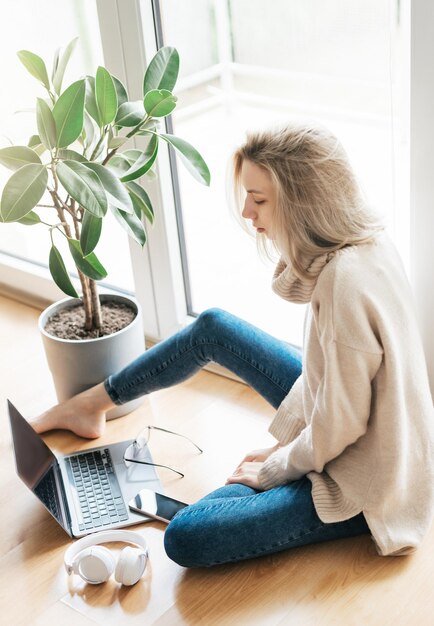 Foto mooie jonge vrouw die haar laptop gebruikt terwijl ze thuis op de vloer zit