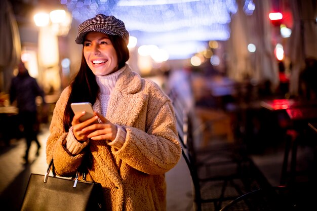 Mooie jonge vrouw die haar mobiele telefoon op straat gebruikt in de kersttijd