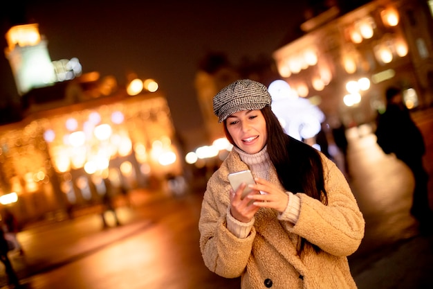 Mooie jonge vrouw die haar mobiele telefoon op straat gebruikt in de kersttijd