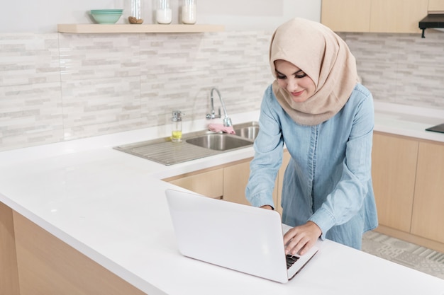 Mooie jonge vrouw die hijab dragen die voedselrecept zoeken op laptop