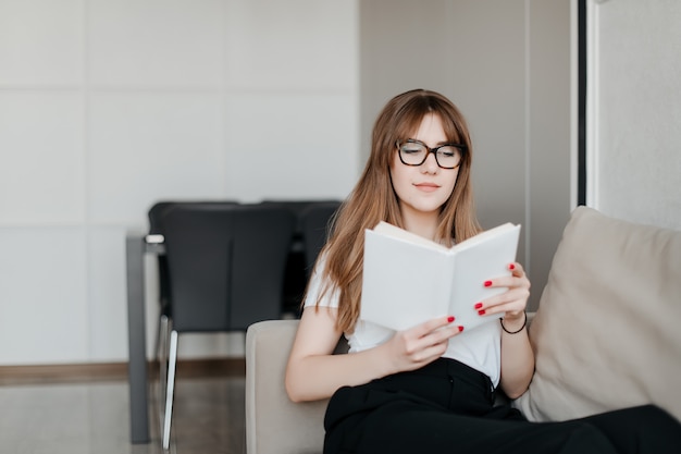 Mooie jonge vrouw die in glazen boek lezen die thuis op laag in flat bestuderen