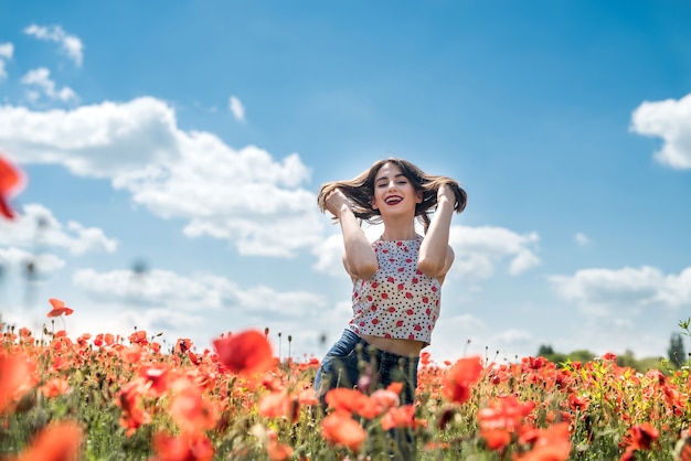 Mooie jonge vrouw die in papavergebied op een de zomerdag loopt