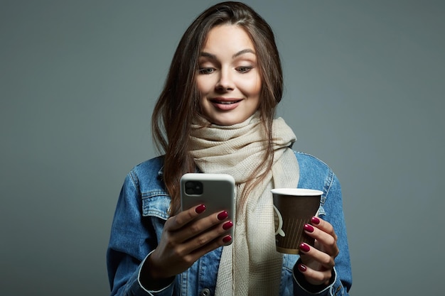 Mooie jonge vrouw die koffie drinkt en naar het telefoonscherm kijkt