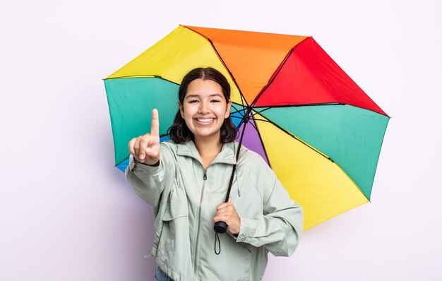 Mooie jonge vrouw die lacht en er vriendelijk uitziet, met nummer één. regen en paraplu concept