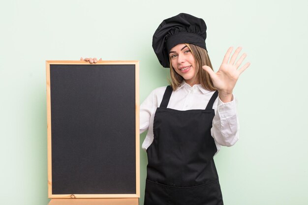 Mooie jonge vrouw die lacht en er vriendelijk uitziet, met nummer vijf. chef-kok met schoolbord