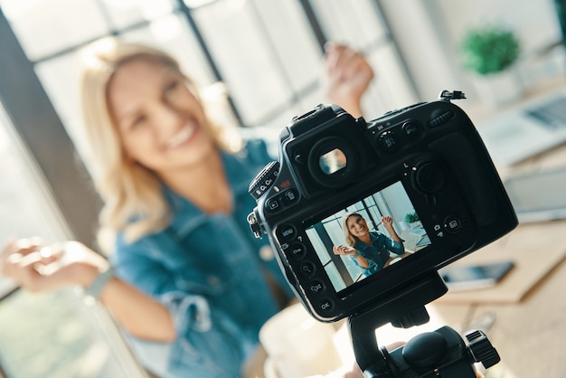 Mooie jonge vrouw die lacht en gebaren maakt terwijl ze voor de digitale camera zit