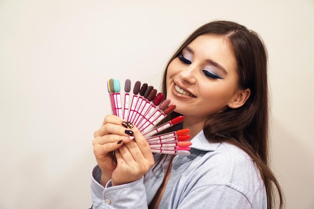 Mooie jonge vrouw die lacht, met een manicure en pedicure nagellak palet in een hand. Cosmetische producten. Schoonheidssalon.