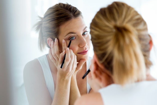 Mooie jonge vrouw die make-up doet dichtbij spiegel thuis.