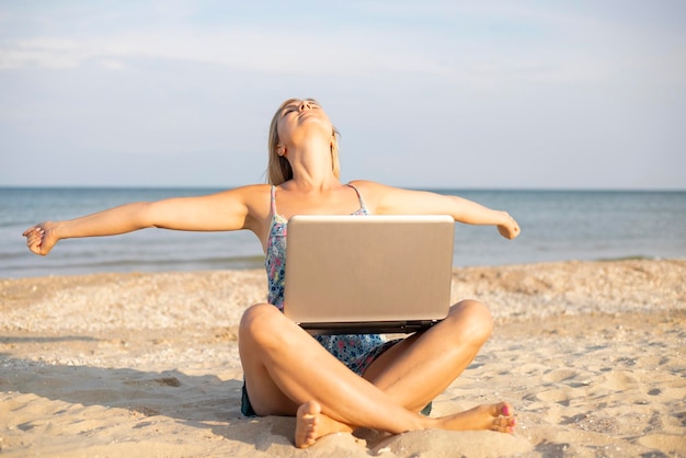 Mooie jonge vrouw die met een laptop aan het tropische strand werkt.