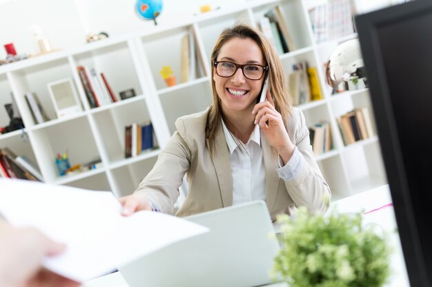 Foto mooie jonge vrouw die met haar mobiele telefoon werkt in haar kantoor.