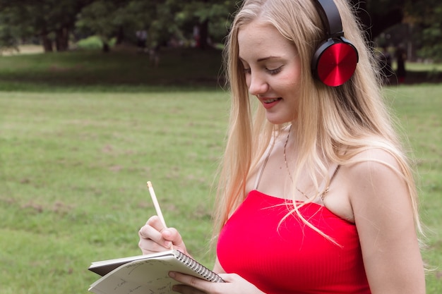 Mooie jonge vrouw die met nota schrijft bij park