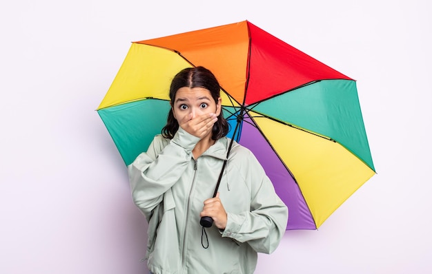 Mooie jonge vrouw die mond bedekt met handen met een geschokt. regen en paraplu concept