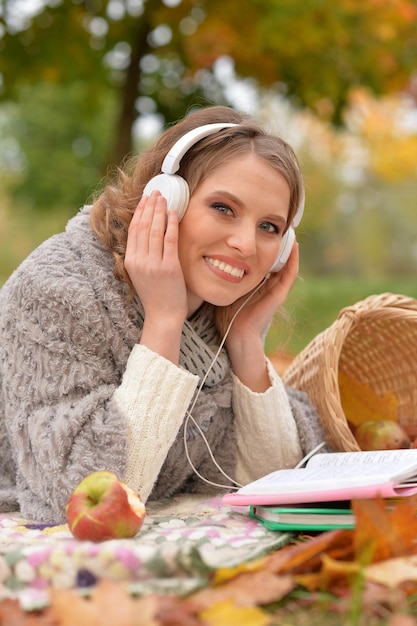 Mooie jonge vrouw die muziek luistert terwijl ze in het herfstpark rust