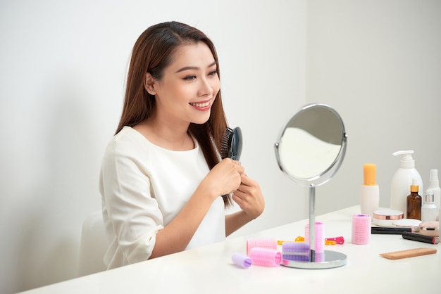 Mooie jonge vrouw die naar haar spiegelbeeld kijkt en haar lange haar borstelt