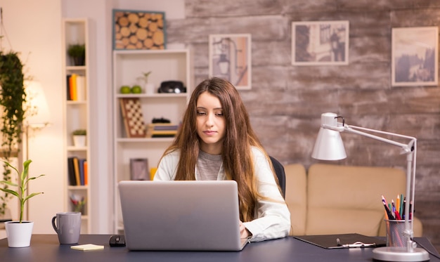 Mooie jonge vrouw die op laptop in kantoor aan huis werkt. Jonge freelancer die vanuit huis werkt.