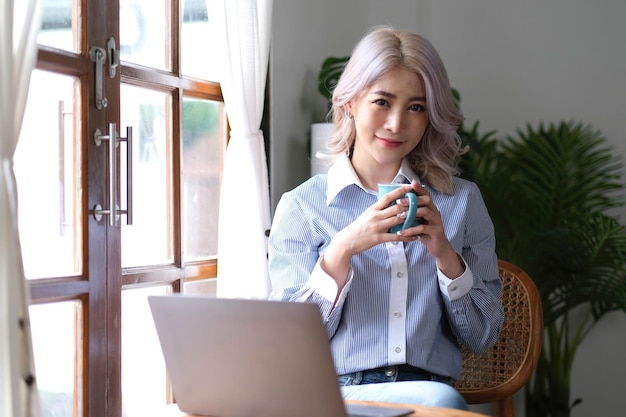 Mooie jonge vrouw die op laptopcomputer werkt terwijl ze in de woonkamer koffie drinkt