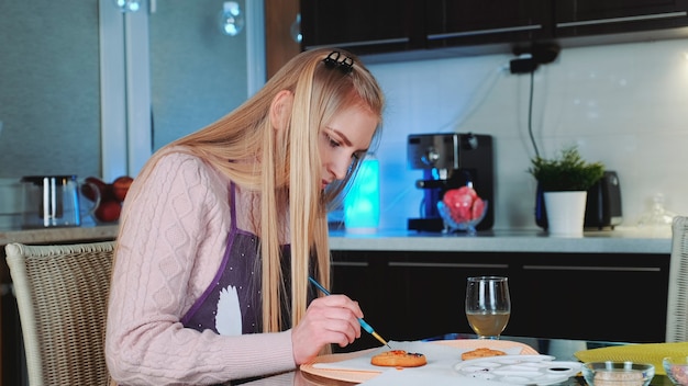 Mooie jonge vrouw die peperkoekkoekjes thuis leert versieren decorate