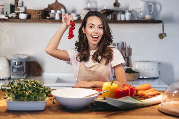 Mooie jonge vrouw die schort draagt die gezonde salade bij de keuken thuis kookt
