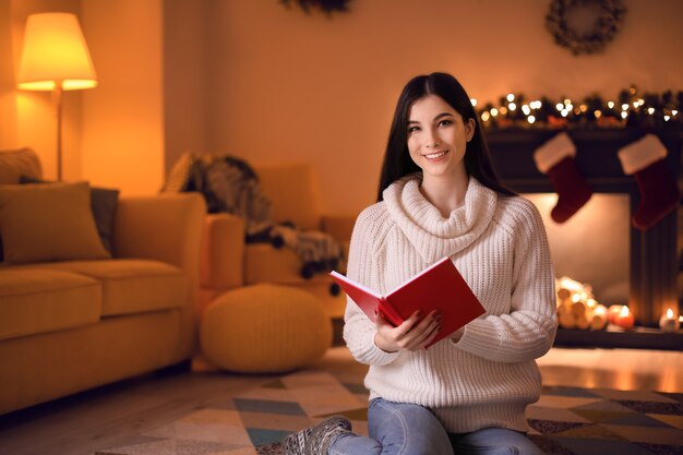 Mooie jonge vrouw die thuis boek leest op kerstavond