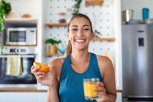 Mooie jonge vrouw die vers sinaasappelsap drinkt in de keuken gezonde voeding gelukkige jonge vrouw met een glas sap en sinaasappel aan tafel in de keuken