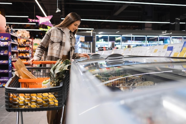 Mooie jonge vrouw die voedsel in supermarkt koopt