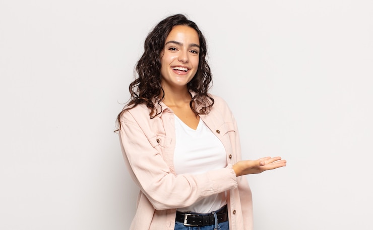 Foto mooie jonge vrouw die vrolijk glimlacht, zich gelukkig voelt en een concept in exemplaarruimte met handpalm toont