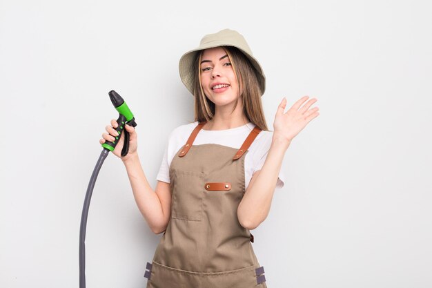 Mooie jonge vrouw die vrolijk lacht, met de hand zwaait, je verwelkomt en begroet. tuinman drenken concept