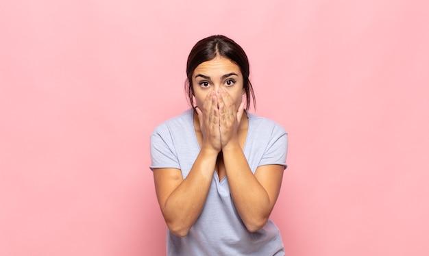 Mooie jonge vrouw die zich ongerust, boos en bang voelt, de mond bedekt met handen, er angstig uitziet en het verprutst