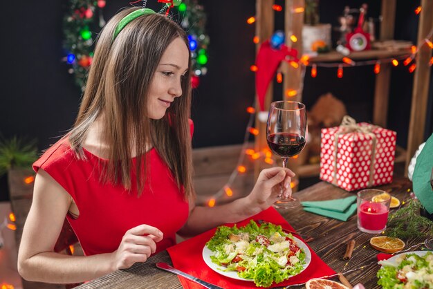 Mooie jonge vrouw dineren aan vakantie tafel met rode geschenkdoos in kerstversiering