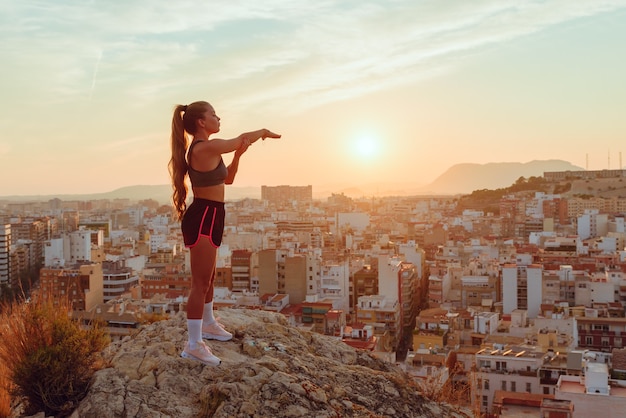 Mooie jonge vrouw doet yoga met uitzicht op de stad bij zonsondergang buitenshuis